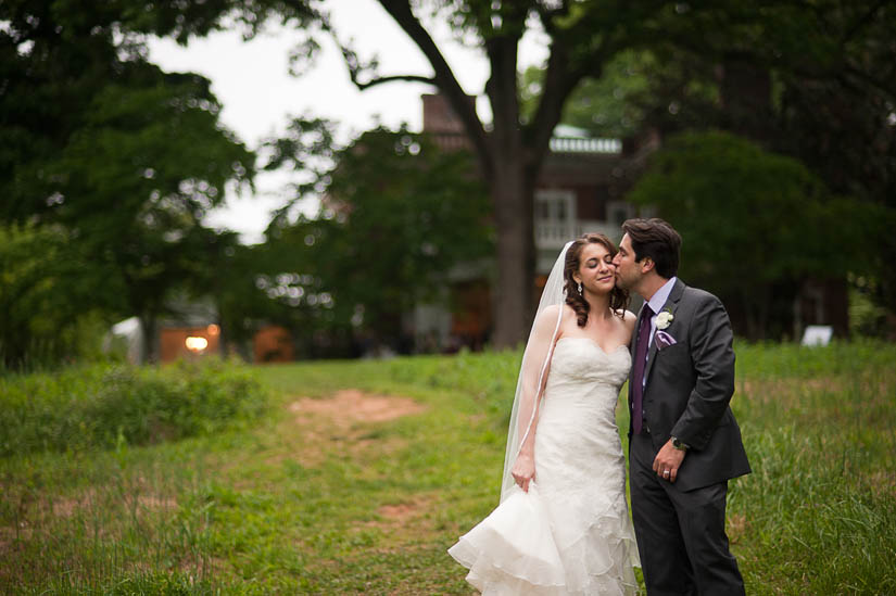 groom kissing bride with woodend in background