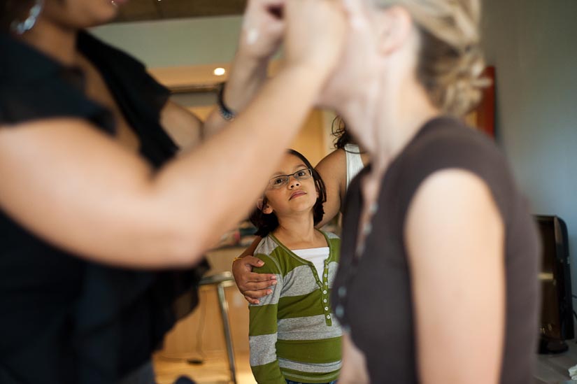 little girl looks on as bride gets makeup done