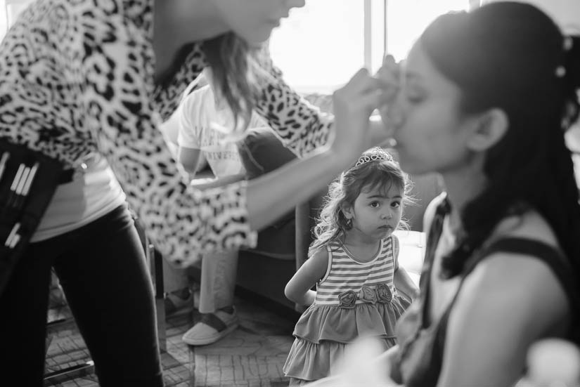 little girl looks on as bride has her makeup done