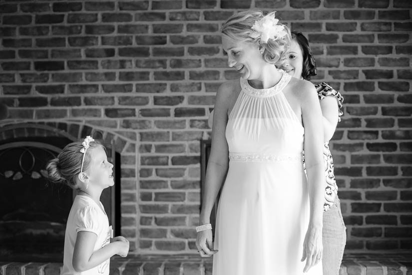 bride and flower girl talking while she puts her dress on